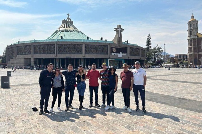 A group of people standing in front of a large building with a green roof and a cross on top. 2