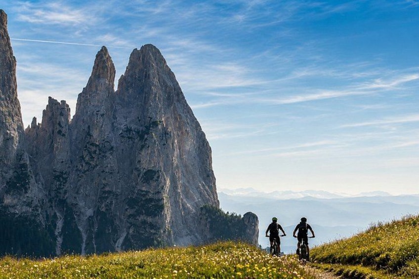 Two cyclists on a trail with a mountainous landscape in the background. 1