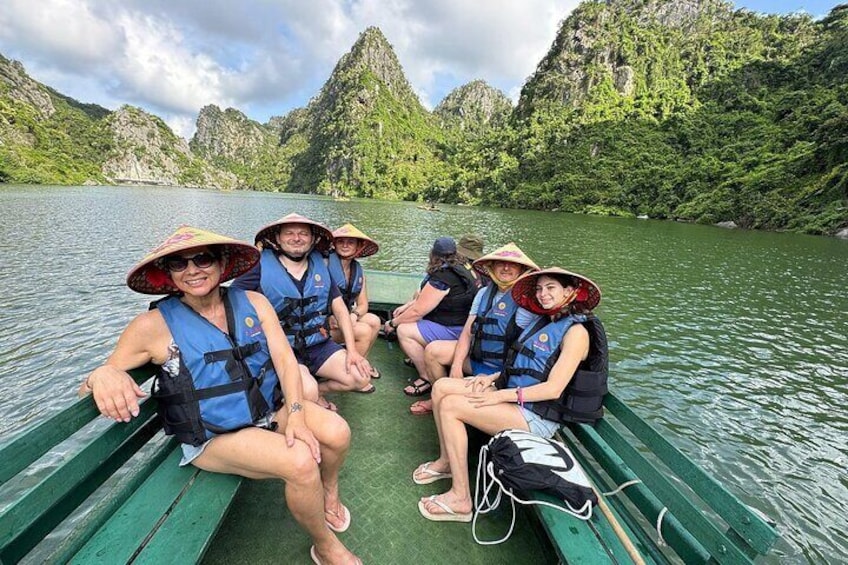 A group of people on a green boat in a river surrounded by green hills. 1