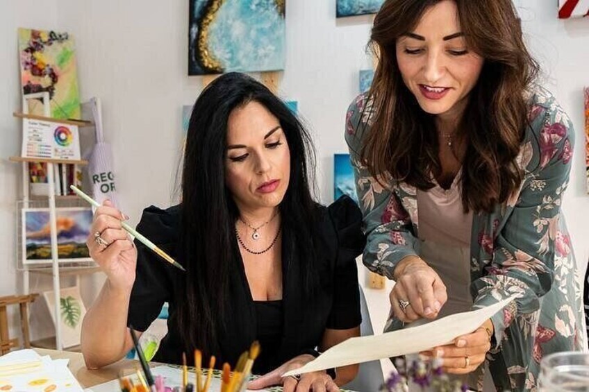 Two people engaged in painting, with art supplies and a palette on the table. 3