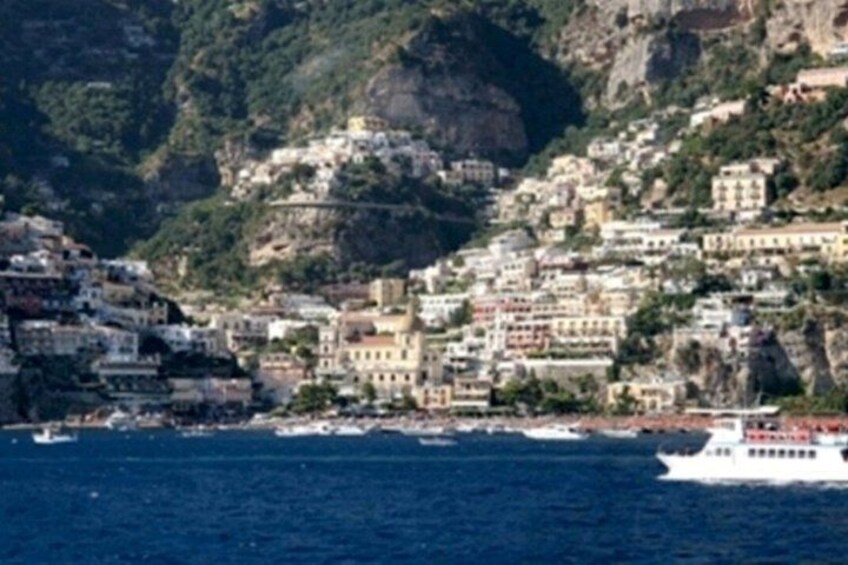 A coastal town with buildings on a hillside, a body of water, and a boat. 1
