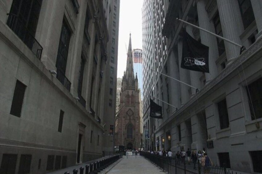 A street with tall buildings, a church spire, and flags. 1