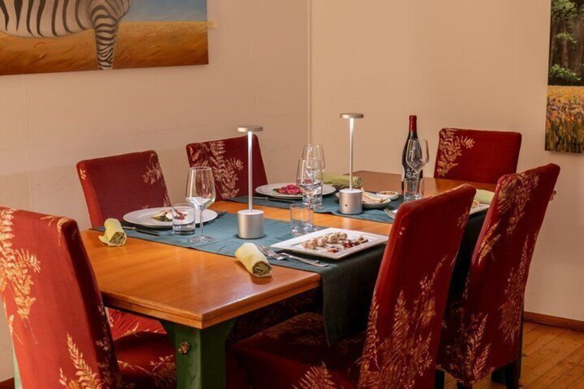 A dining table set with plates, glasses, and a bottle, surrounded by red upholstered chairs. 4