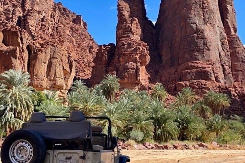 A desert landscape with red rock formations, palm trees, and a parked off-road vehicle. 4