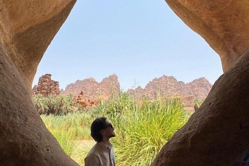 A person looking through a natural rock arch at a desert landscape with red rock formations and green vegetation. 3