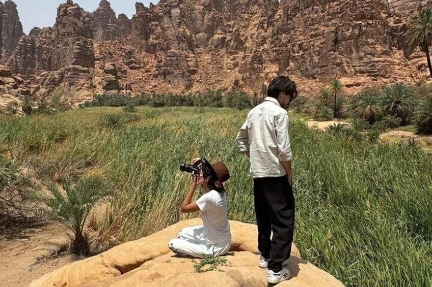 A person taking a photograph with a camera, another person standing nearby, and a rocky desert landscape with sparse vegetation. 2