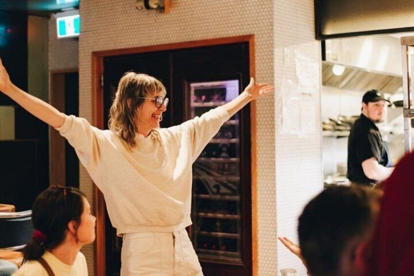 A person in a white shirt and pants standing with arms outstretched in a room with a tiled wall and a door in the background. 3