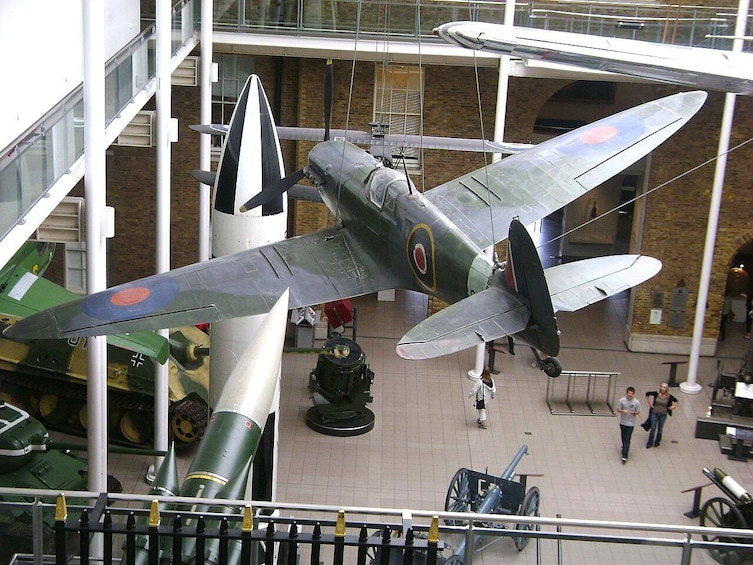 L’intérieur d’un musée, avec un avion de chasse de la Seconde Guerre mondiale suspendu au centre, entouré d’autres pièces exposées sur le thème militaire. 2