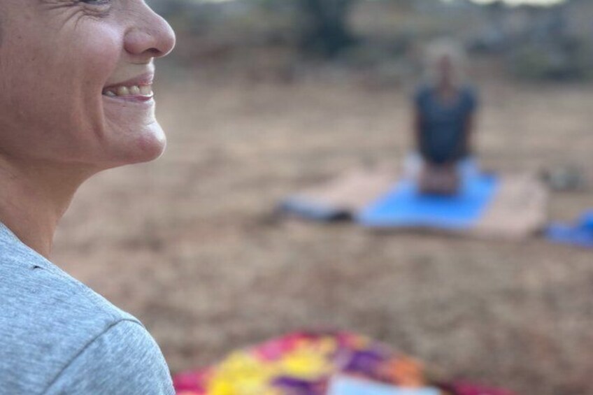 A person in a grey top and a colorful blanket, with another person in the background on a blue mat. 5