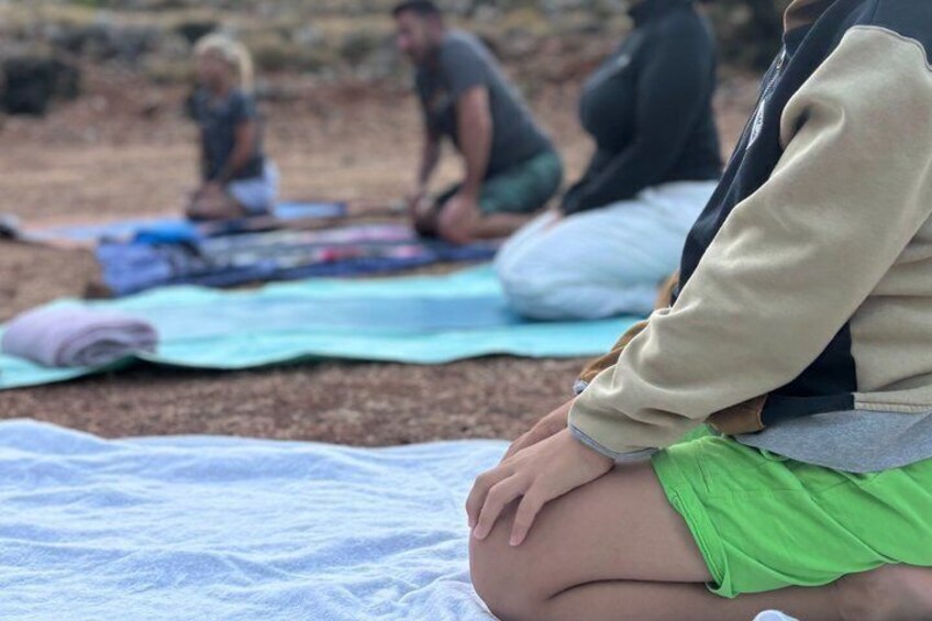 A person sitting on a mat outdoors, with others in the background. 4