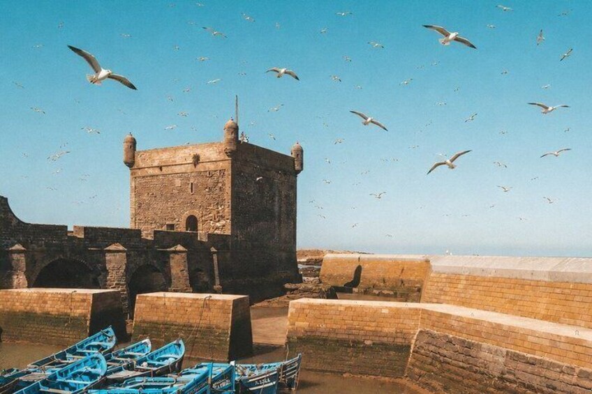 A historic stone tower, boats, and seagulls flying in the sky. 3