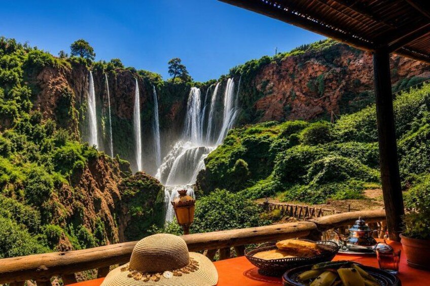 A dining table with food and a hat, overlooking a waterfall. 2