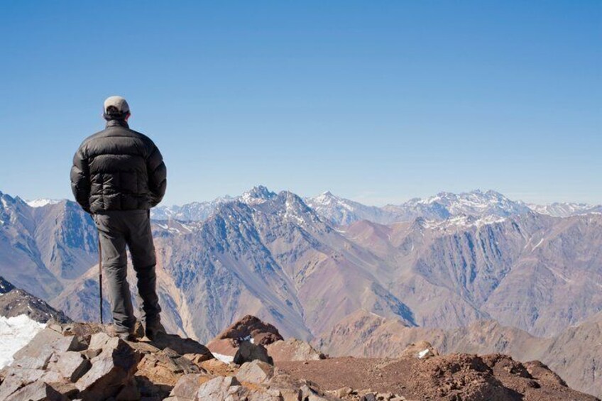 A person standing on a rocky mountain peak overlooking a range of snow-capped mountains. 2