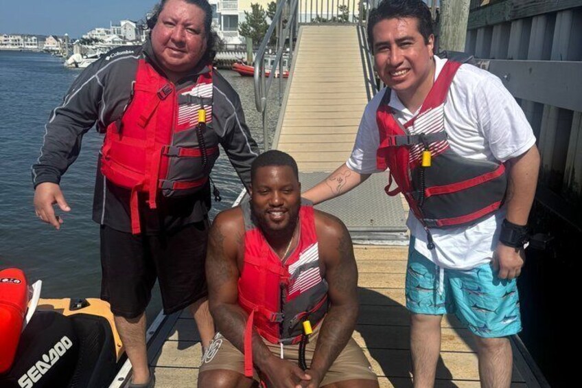 Three people wearing life jackets on a dock by the water. 1