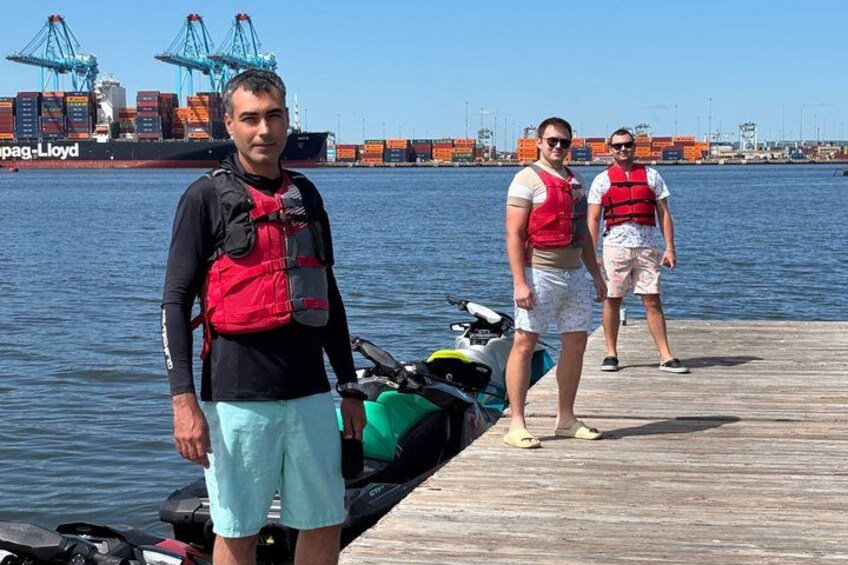A man and a woman on a dock with a boat and a cargo ship in the background. 2