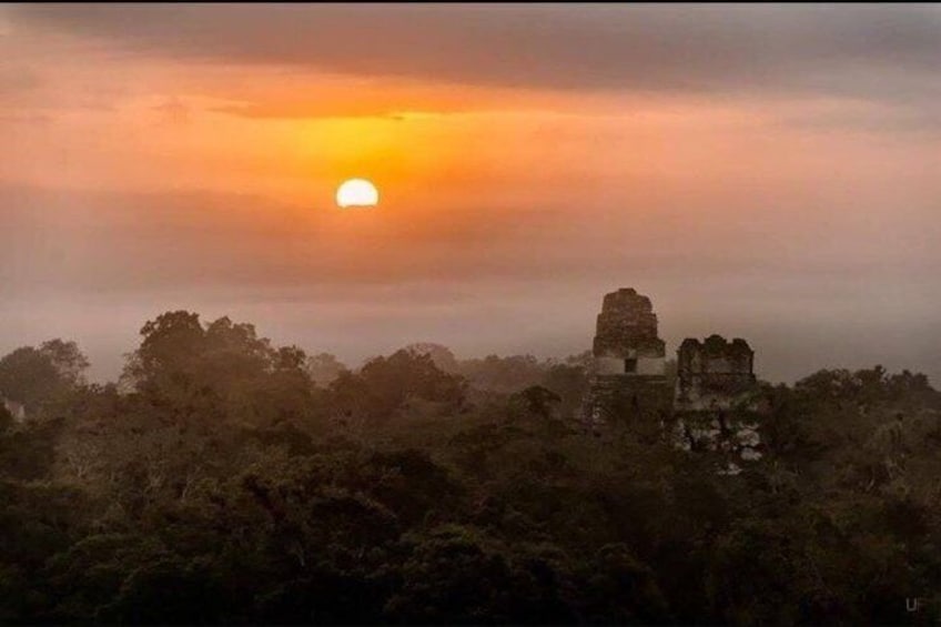 A sunset over a forested area with ancient ruins. 1