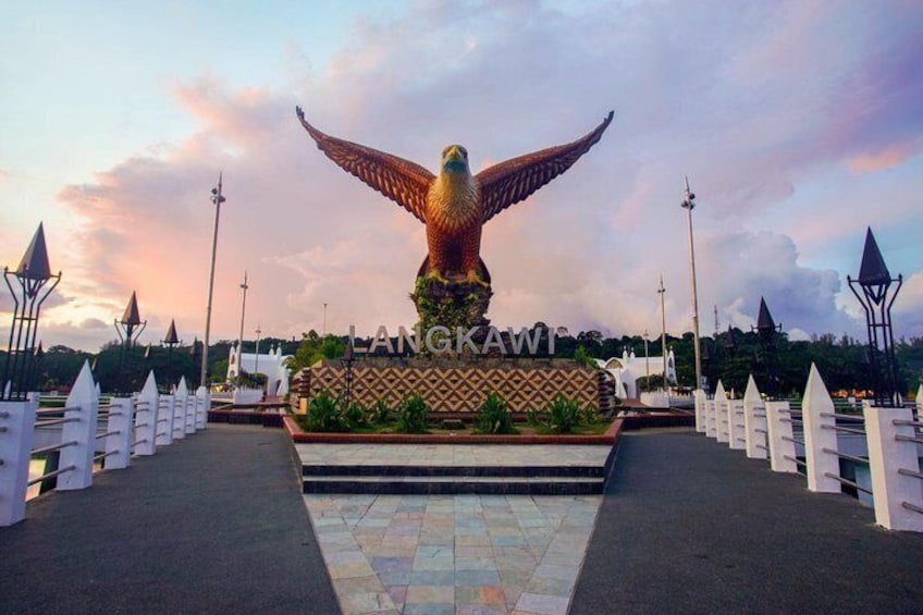 A large golden eagle statue with outstretched wings, a white fence, and a patterned wall with the text 'LANGKAWI' in the foreground. 5