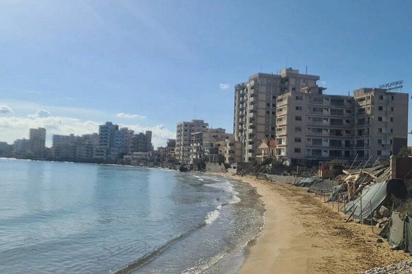 Una playa con arena, mar tranquilo y una hilera de edificios altos al fondo. 5