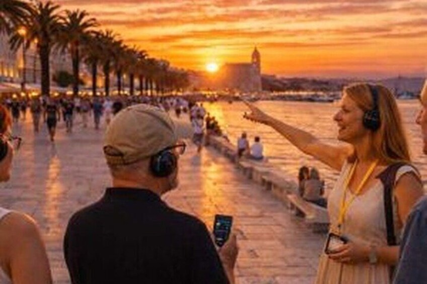 A sunset over a waterfront promenade with palm trees and people walking. 3