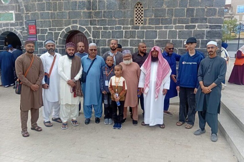A group of people standing in front of a stone building with arched doorways. 2