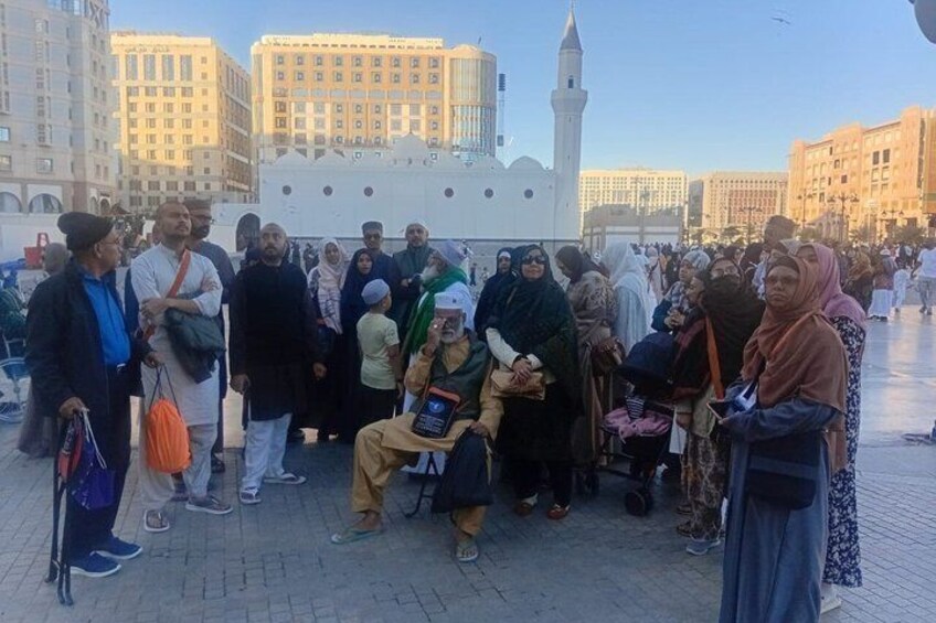 A group of people gathered in an open square with a prominent white building featuring a minaret in the background. 3