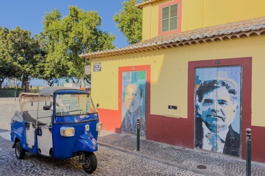 A blue three-wheeled vehicle parked in front of a building with a mural. 3