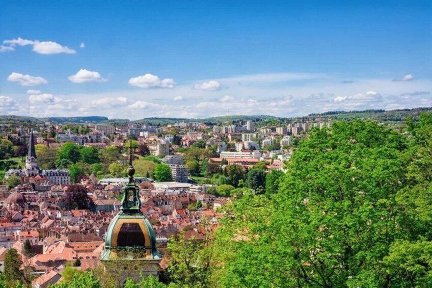 A cityscape with a prominent green-domed structure, dense urban buildings, and a clear blue sky. 3