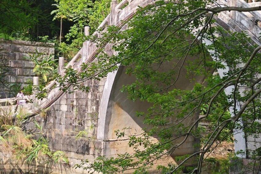 A stone bridge with a curved arch, surrounded by greenery and a stone wall. 2