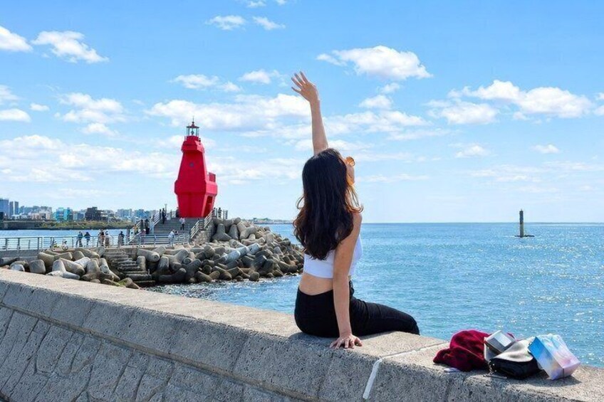A person sitting by a waterfront with a red lighthouse in the background. 1