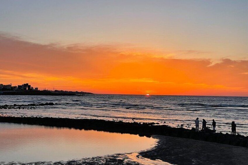 A sunset over a beach with people walking along the shore. 2
