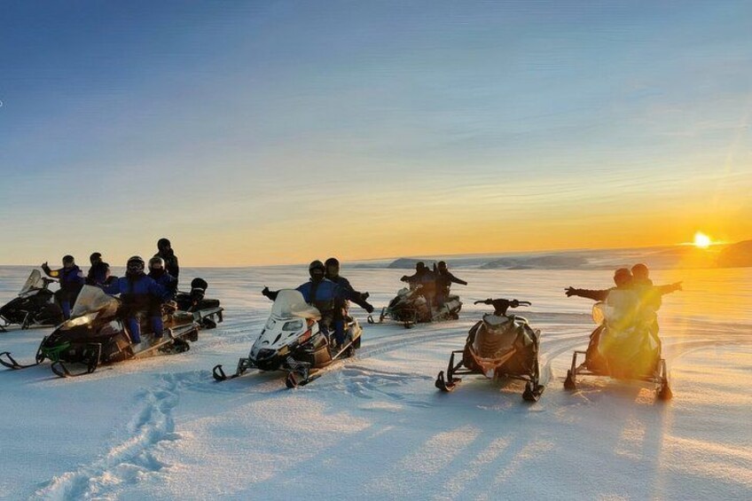A group of people on snowmobiles on a snowy landscape during sunset. 1
