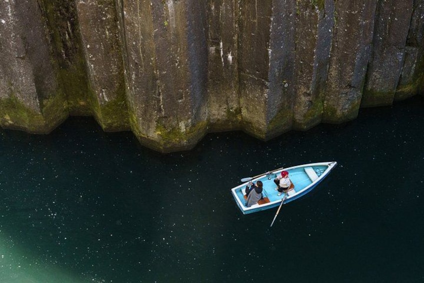 A small boat with two people on a calm body of water, surrounded by large rock formations. 2