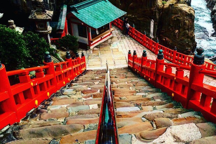 A stone staircase leading up to a temple with red railings and a green roof. 3