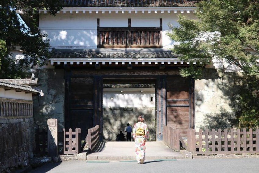 A traditional building with a wooden gate, a stone wall, and a person in traditional attire walking towards the entrance. 4