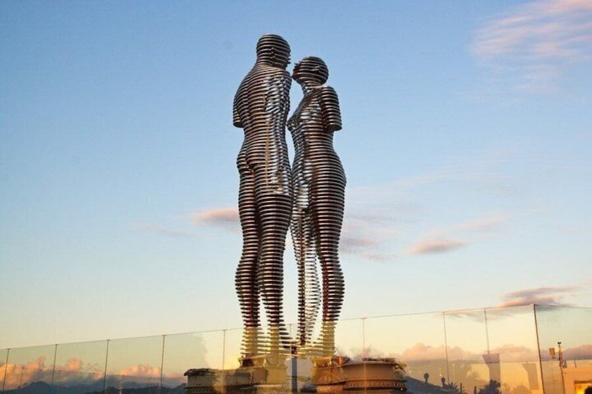 A metallic sculpture of two figures in a standing position, set against a clear sky. 5