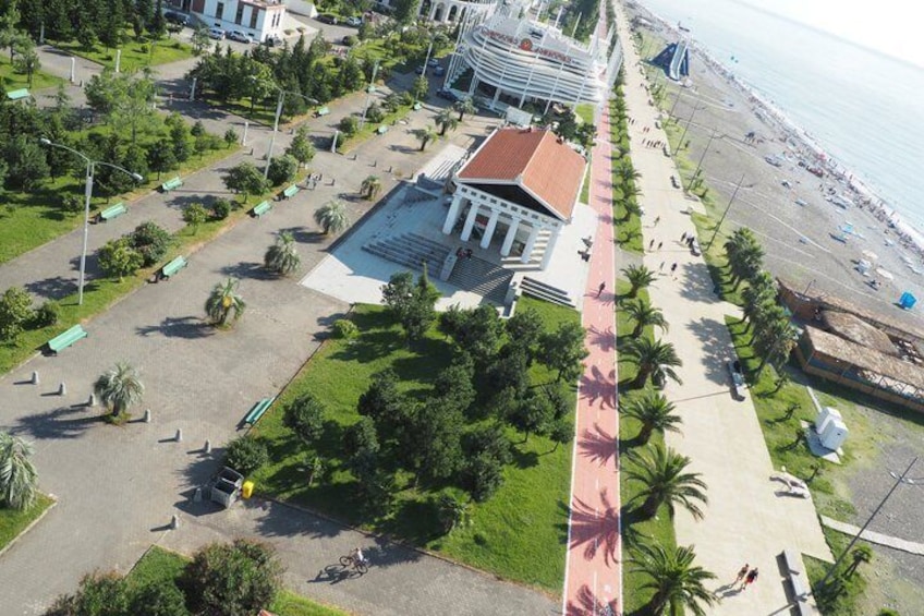 A coastal promenade with a central building, palm trees, and a beach. 4
