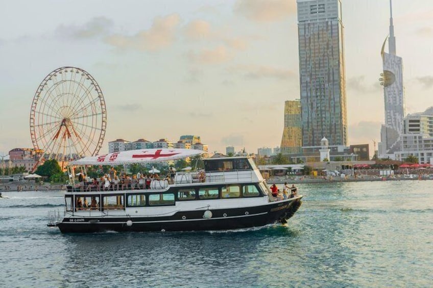 A boat with passengers on a river, a Ferris wheel, and modern skyscrapers in the background. 3