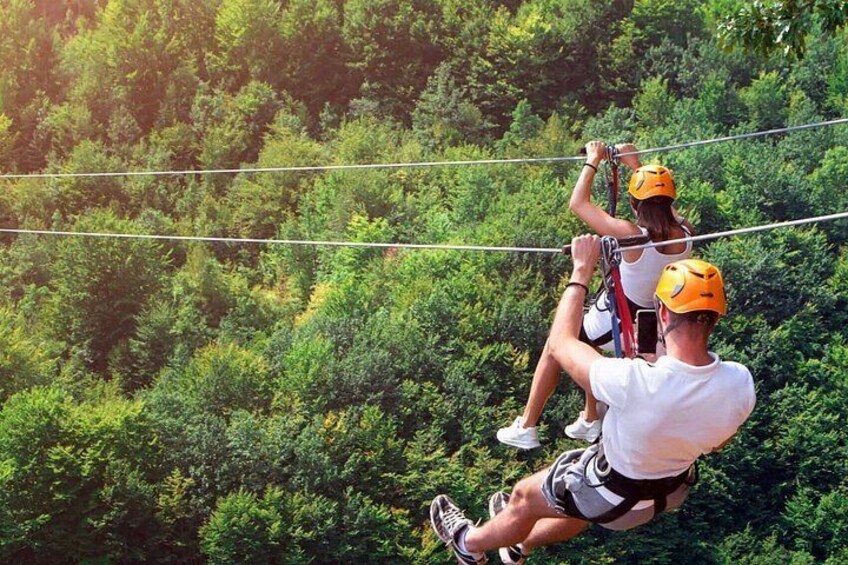 Two people on a zip line with a forested landscape in the background. 3