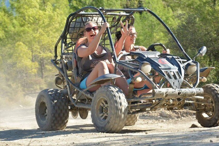 Two people in a dune buggy on a sandy terrain with trees in the background. 2