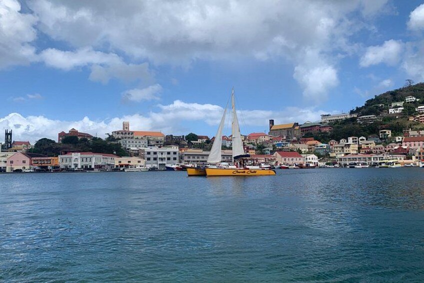 A coastal town with a sailboat, buildings, and a hilly landscape. 1