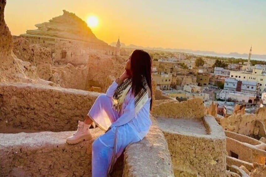 A person sitting on ancient ruins during sunset with a cityscape in the background. 2