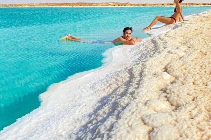 A person lying on a white, textured surface by a turquoise pool. 3