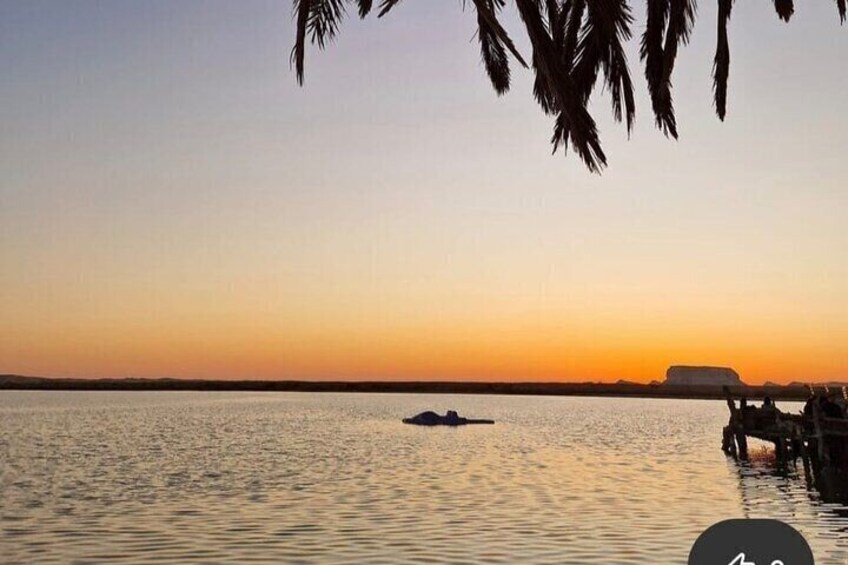 A calm body of water at sunset with a boat and a distant landmass. 4