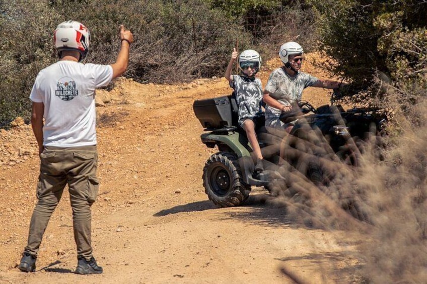 A person directing an ATV on a dirt path, with a child seated on the back. 1