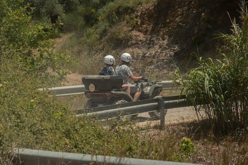 Two individuals on an ATV navigating a dirt path surrounded by vegetation. 2