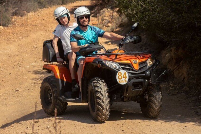 Two people on an orange ATV with a speed limit sign of 84 km/h. 1