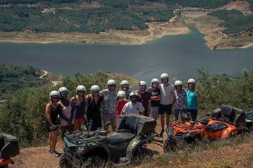 A group of people with ATVs on a hillside overlooking a lake. 2