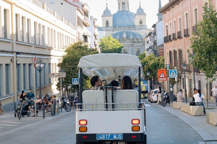 A white bus with passengers, a blue street sign, and a building with a dome in the background. 2