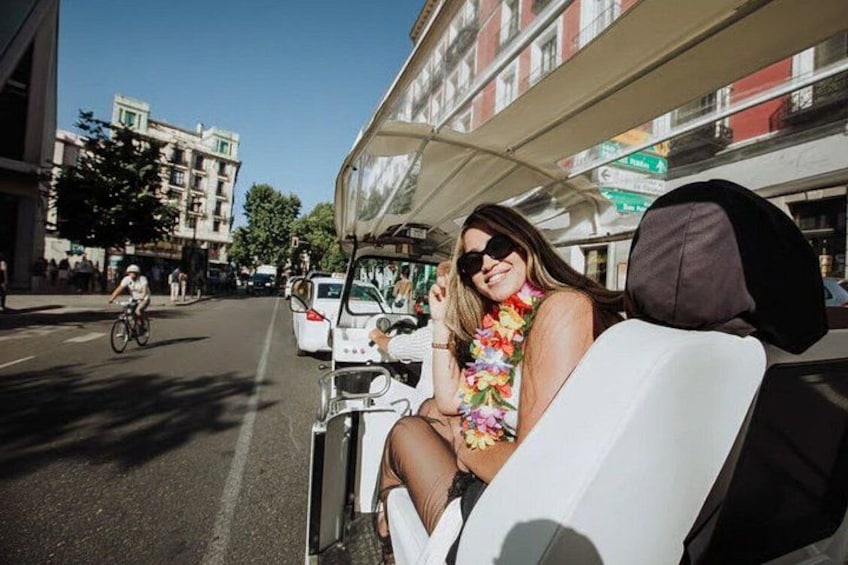 A person in a floral top sitting in a vehicle with a black cap on the seat. 1