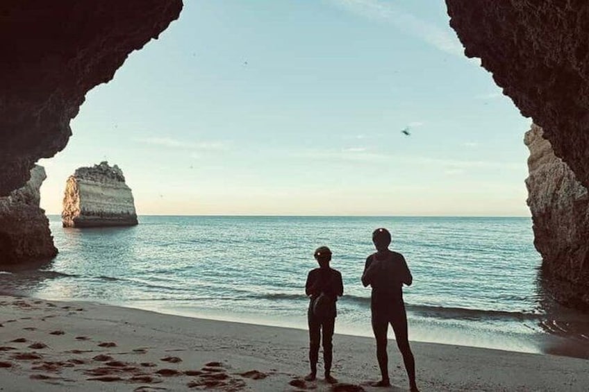 Two people standing on a beach, looking at a rock formation in the water. 3